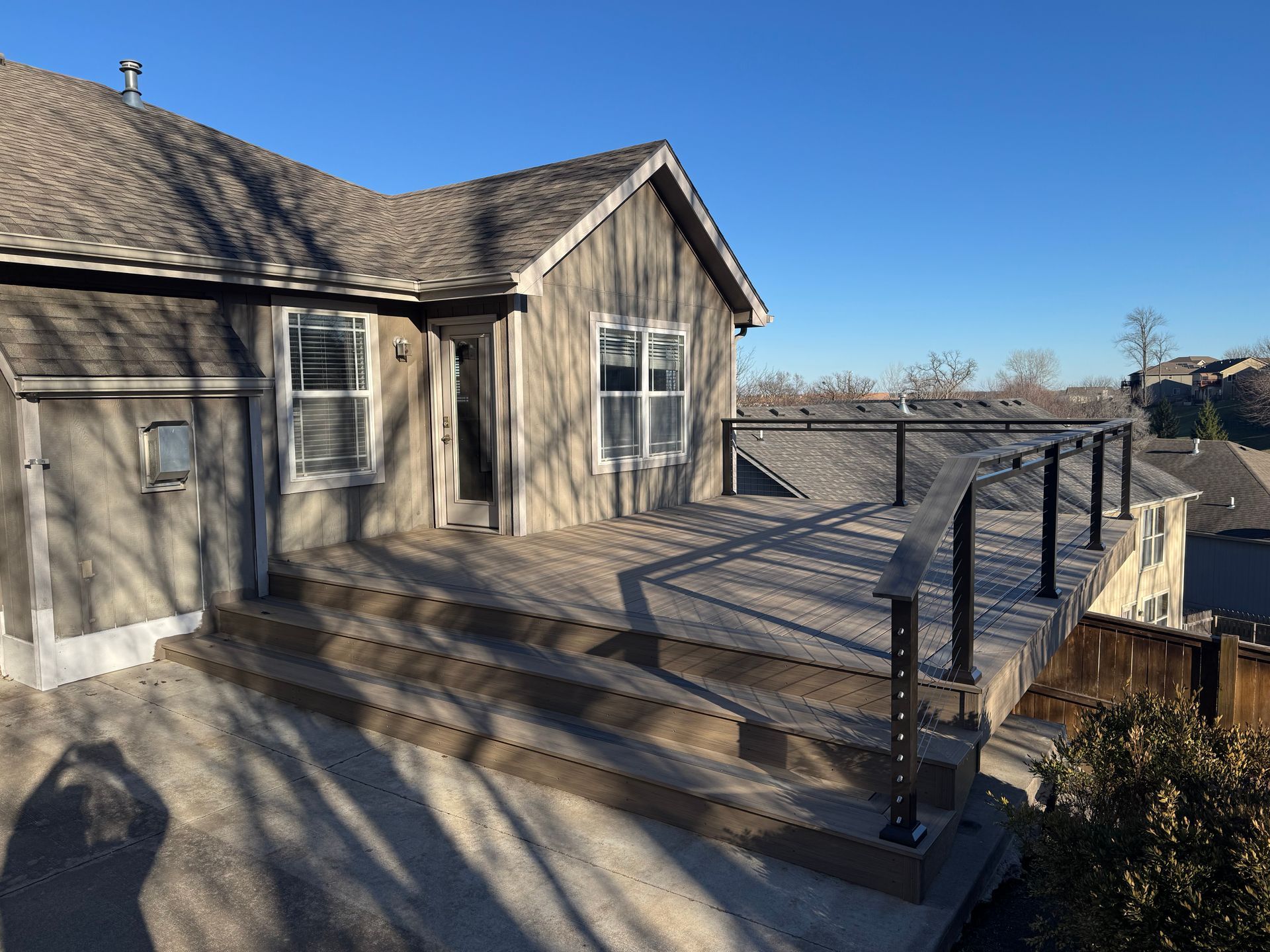 House with wooden deck and black railing under a clear blue sky