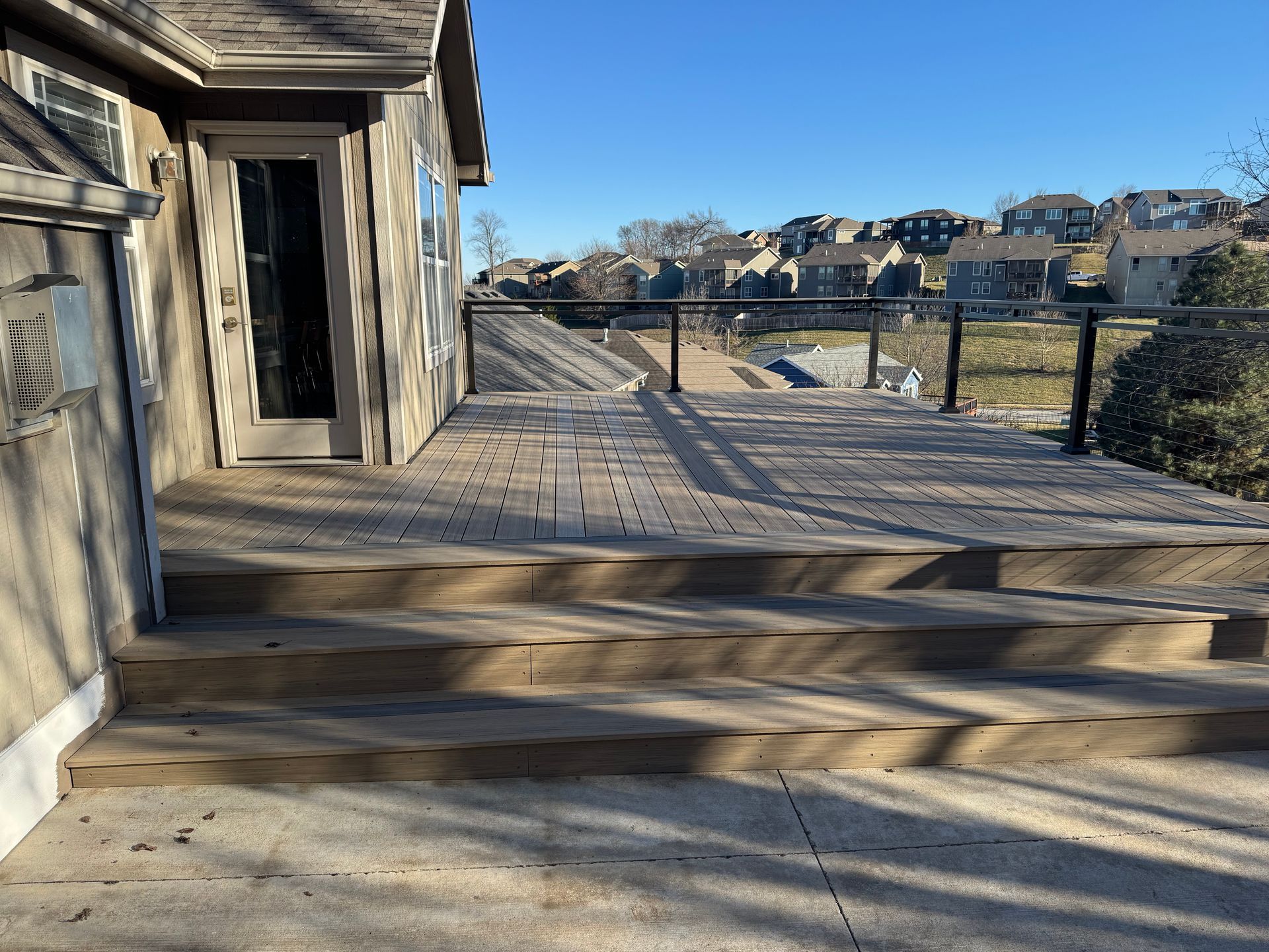 Wooden deck and steps beside a weathered building, overlooking a fenced field and distant houses.