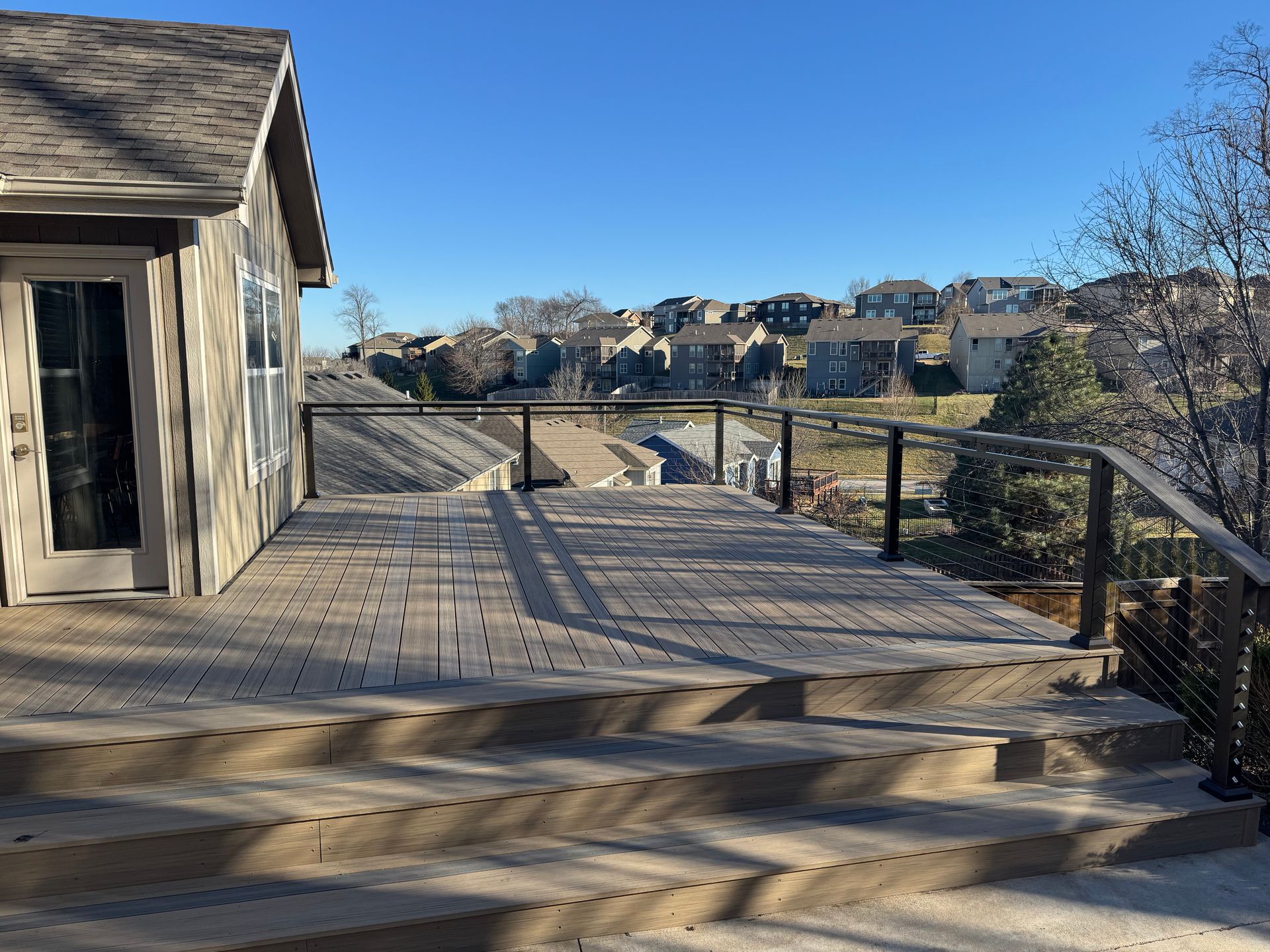 Wooden deck with steps and railing overlooking a hillside neighborhood under a clear blue sky