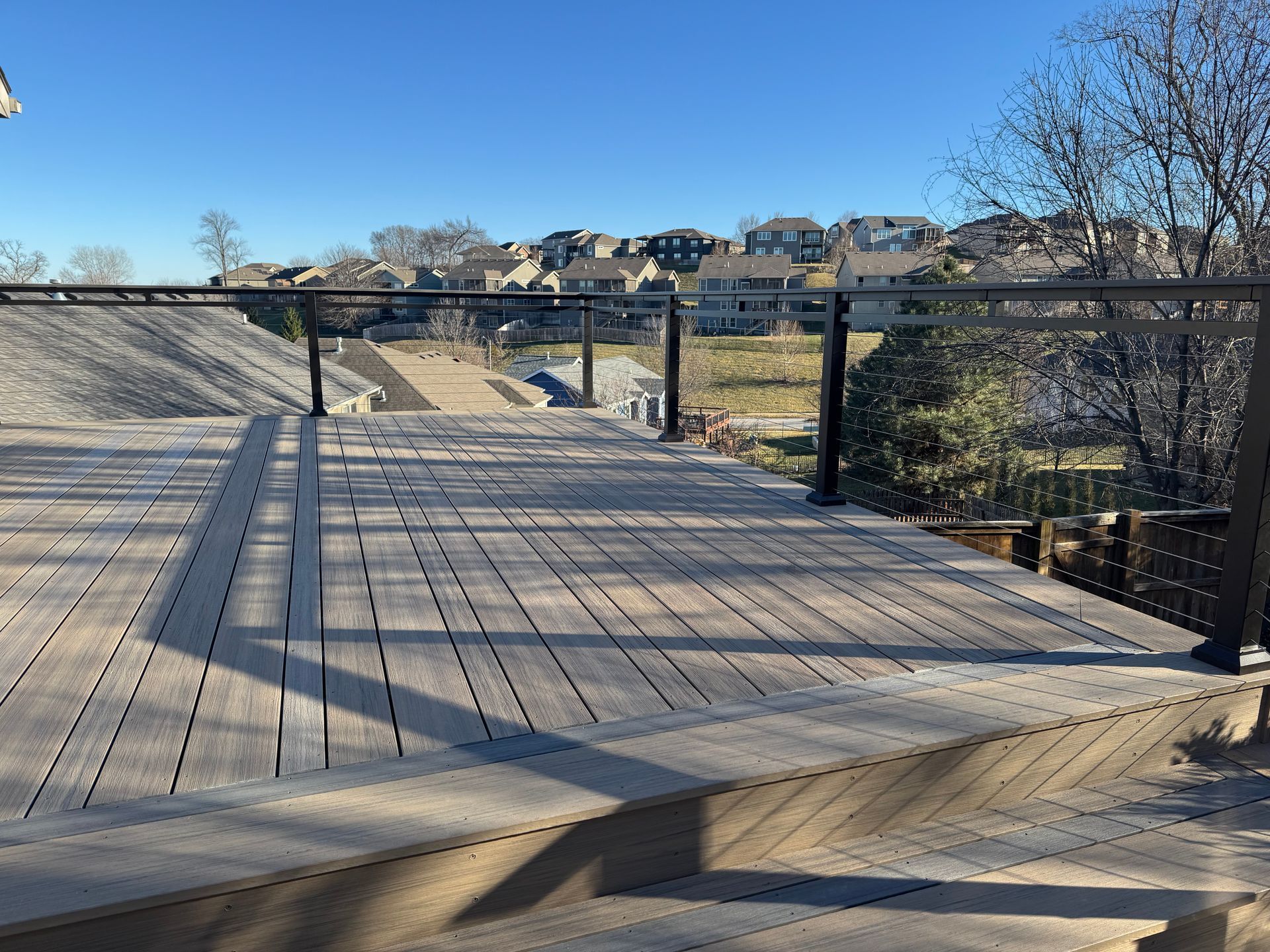 Wooden boardwalk and railings overlooking a grassy drainage channel under a clear blue sky.