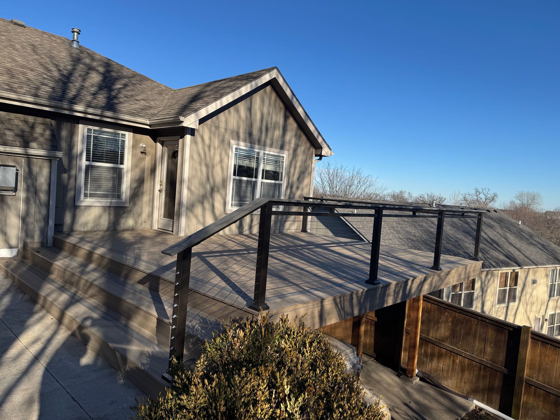 Wooden deck and railing beside a house on a sunny day, with mountains in the background