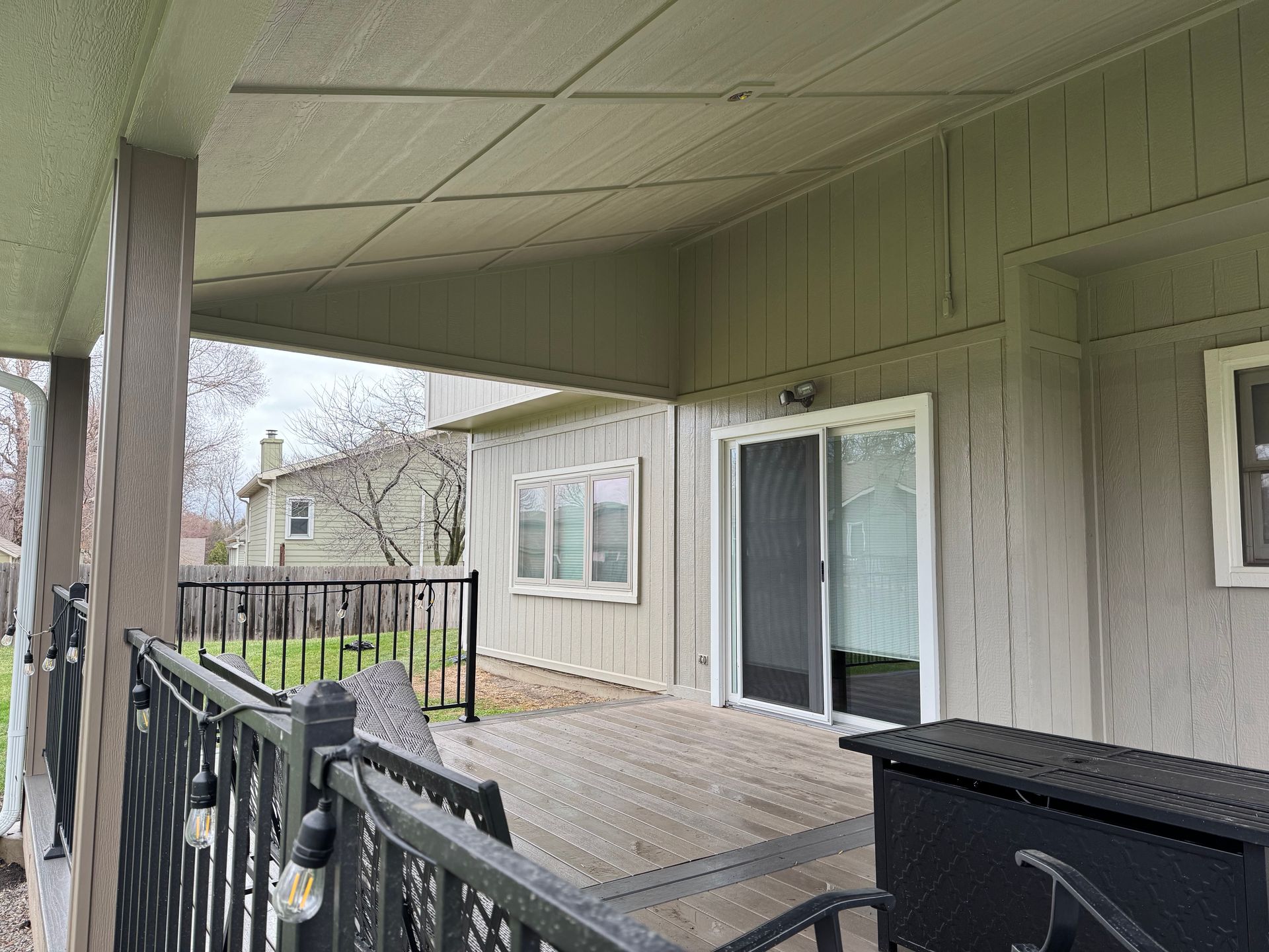 Covered apartment balcony with black railings, wooden deck, and sliding glass doors overlooking a grassy area