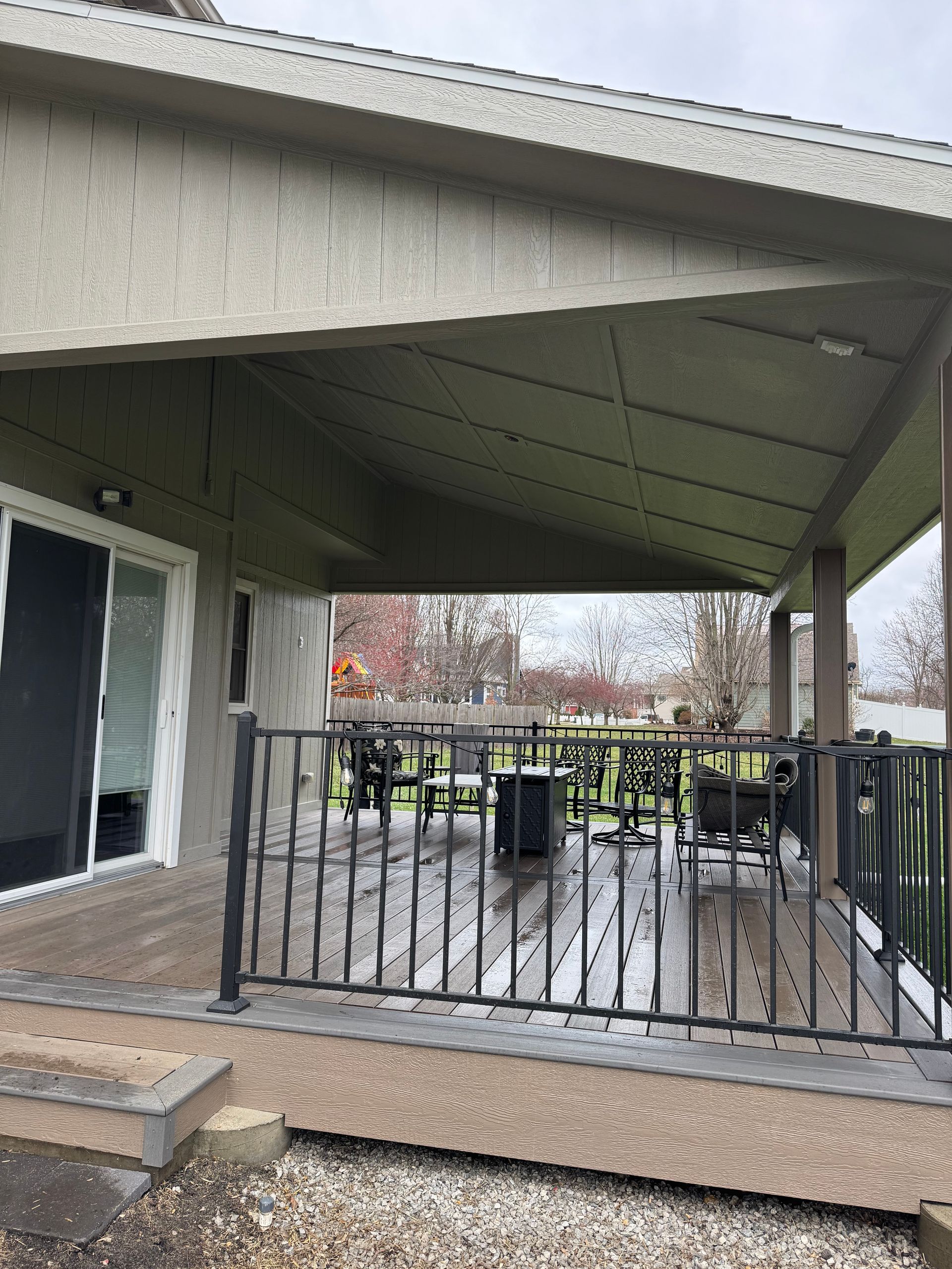 Covered backyard patio with black railing, concrete floor, and a sliding glass door.