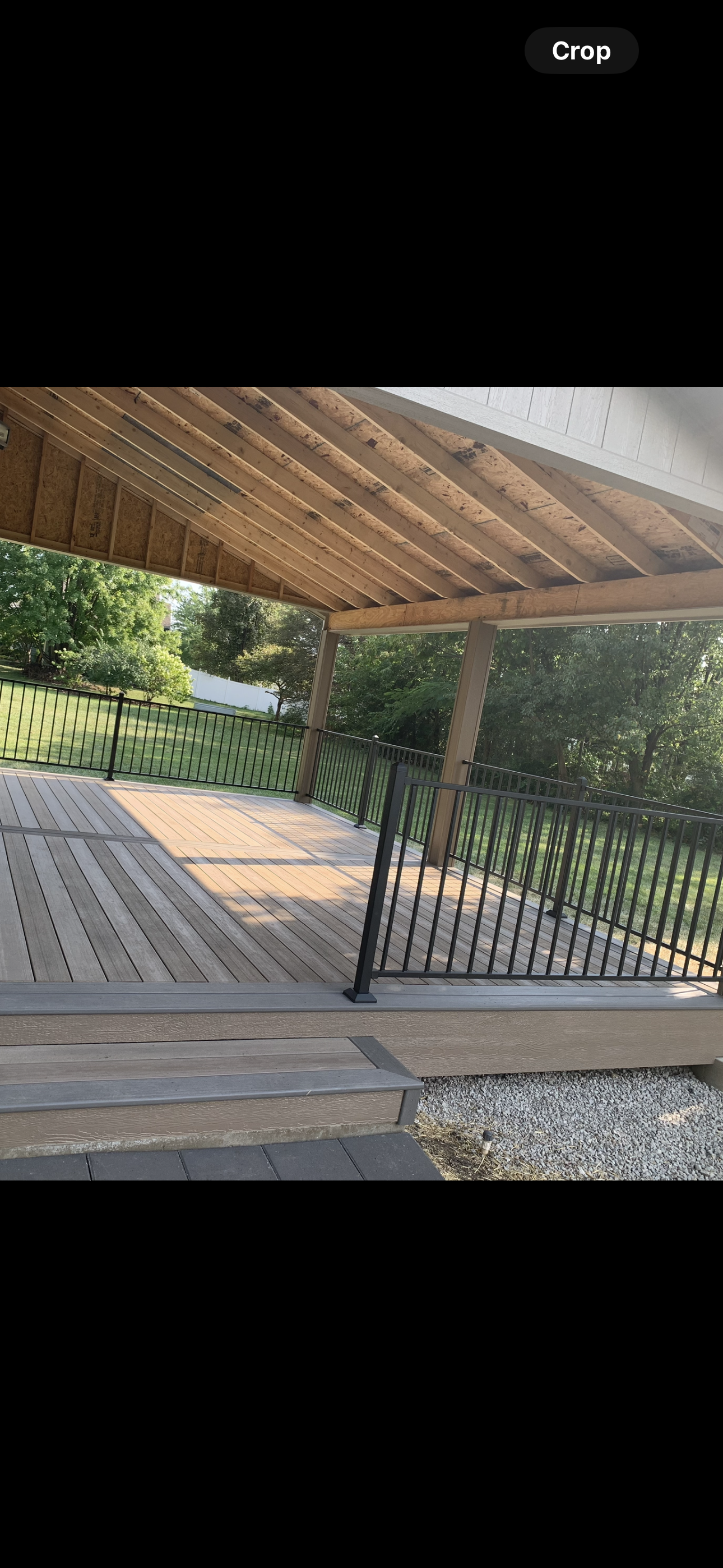 Covered outdoor patio with wooden roof, black metal fencing, and a grassy yard beyond.