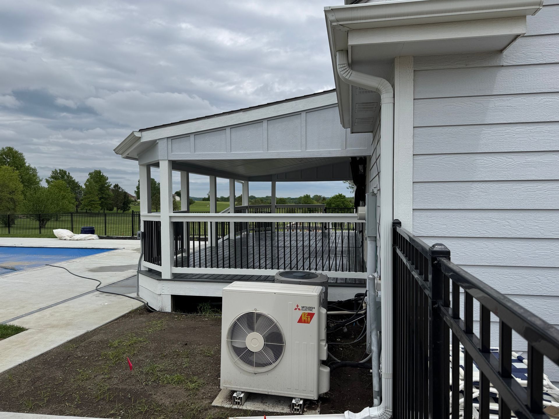 White porch beside a swimming pool, with an outdoor AC unit in front and a black railing on the right.