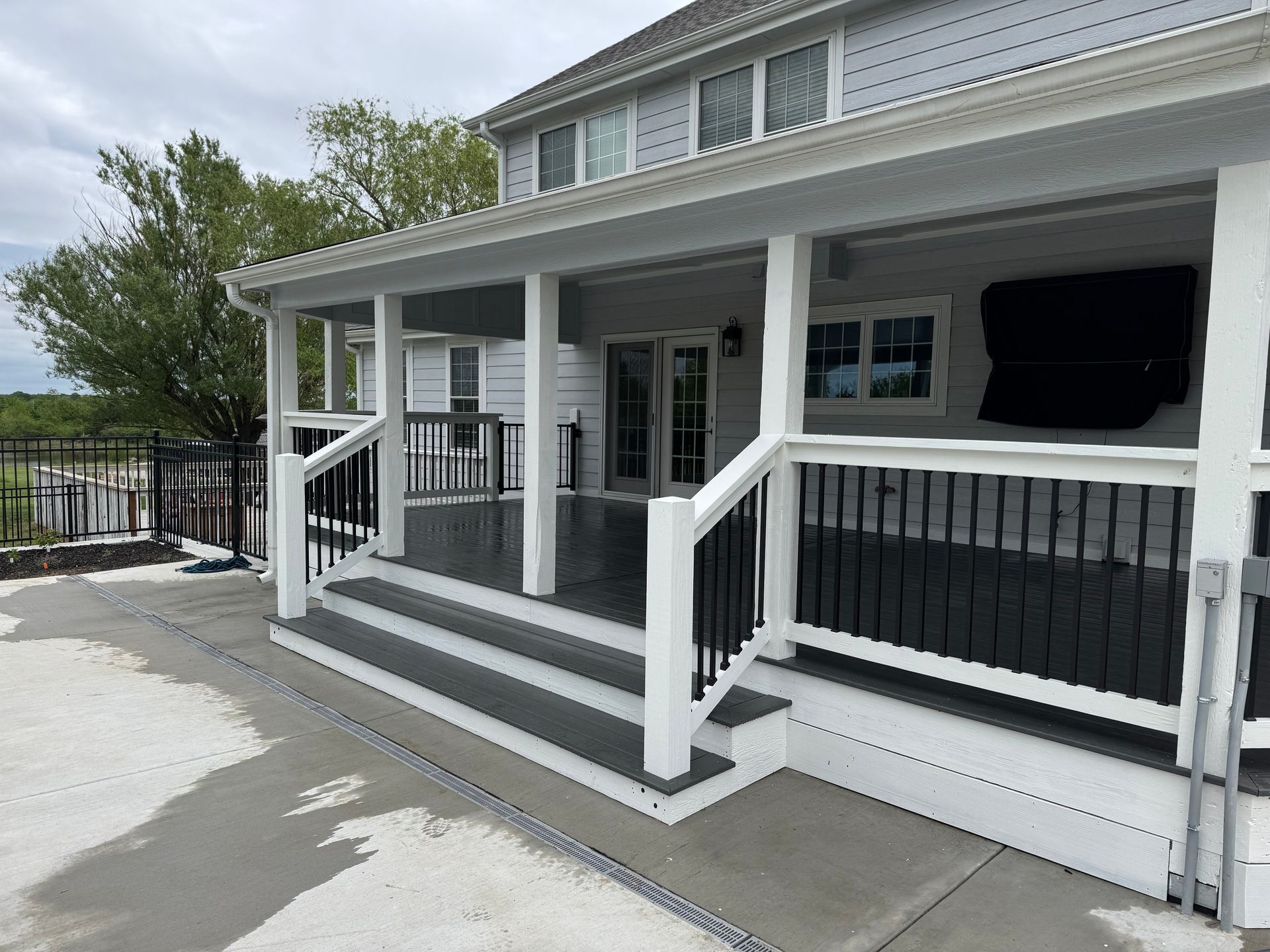 Front porch with white railings, steps, and covered seating area on a gray house.