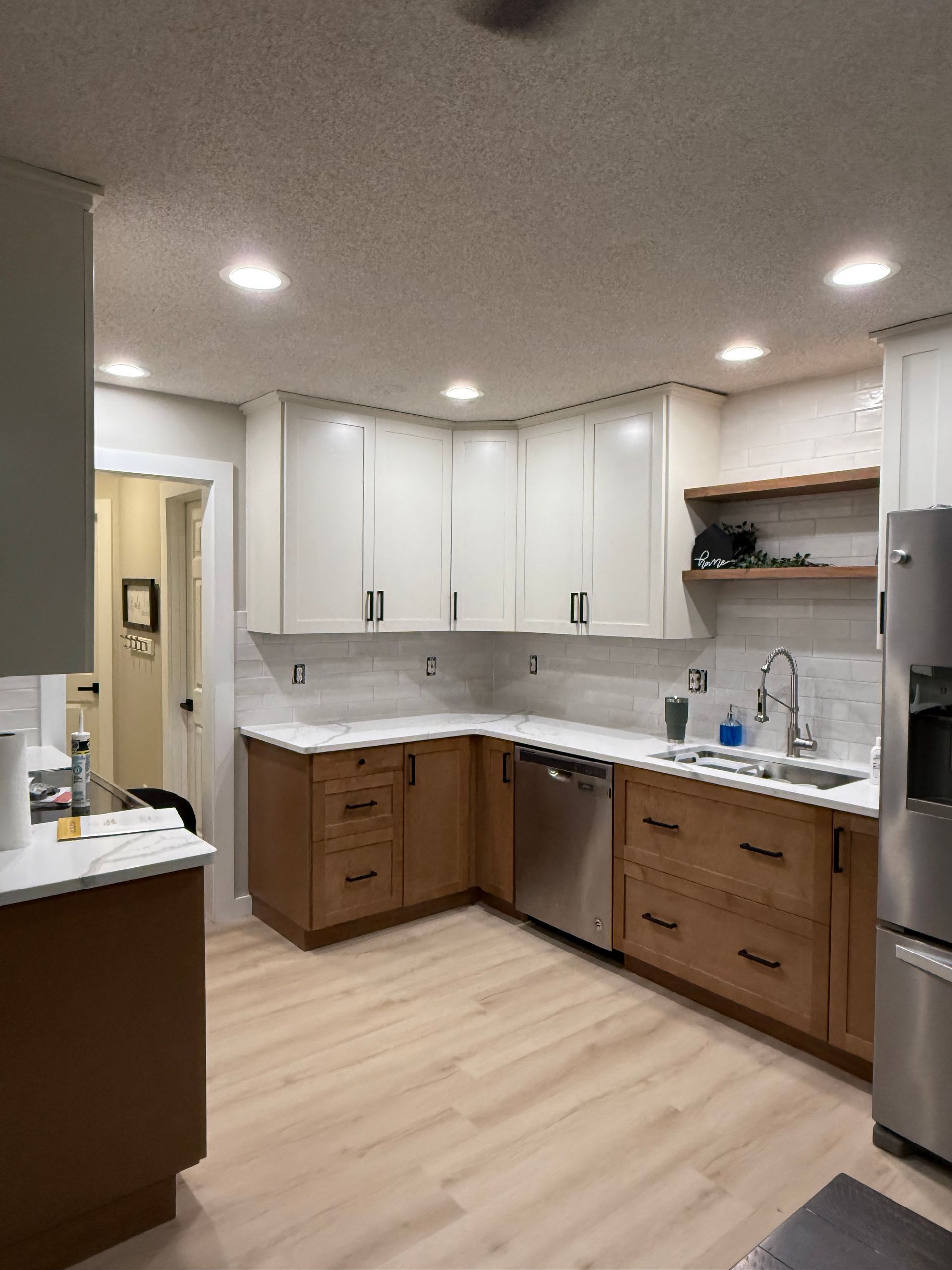 Modern kitchen with white cabinets, wood lower drawers, stainless dishwasher, and light wood flooring.