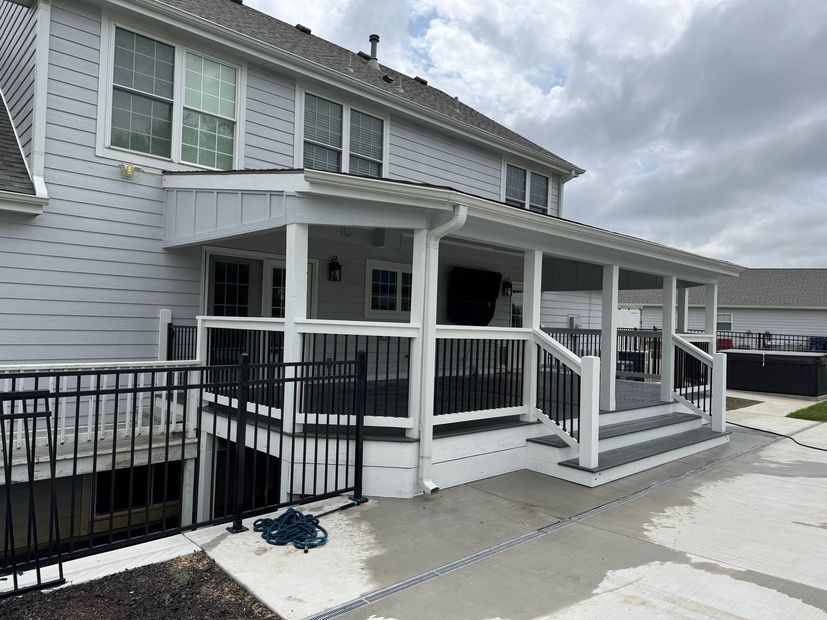 White two-story house with a covered porch, black railings, and a waterfront view under cloudy skies