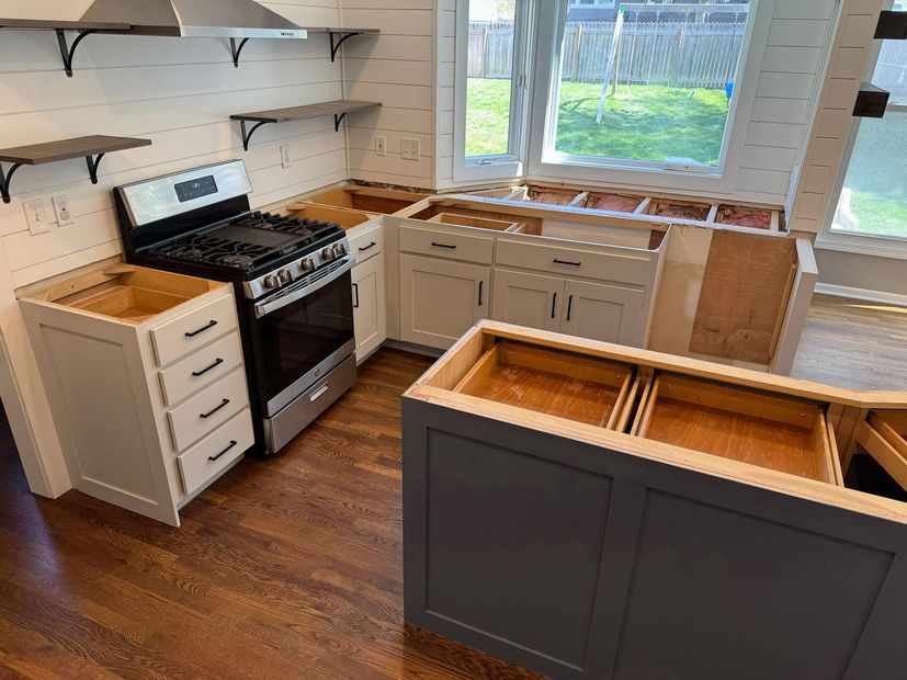 Partially renovated kitchen with white cabinets, black stove, and unfinished island under a window