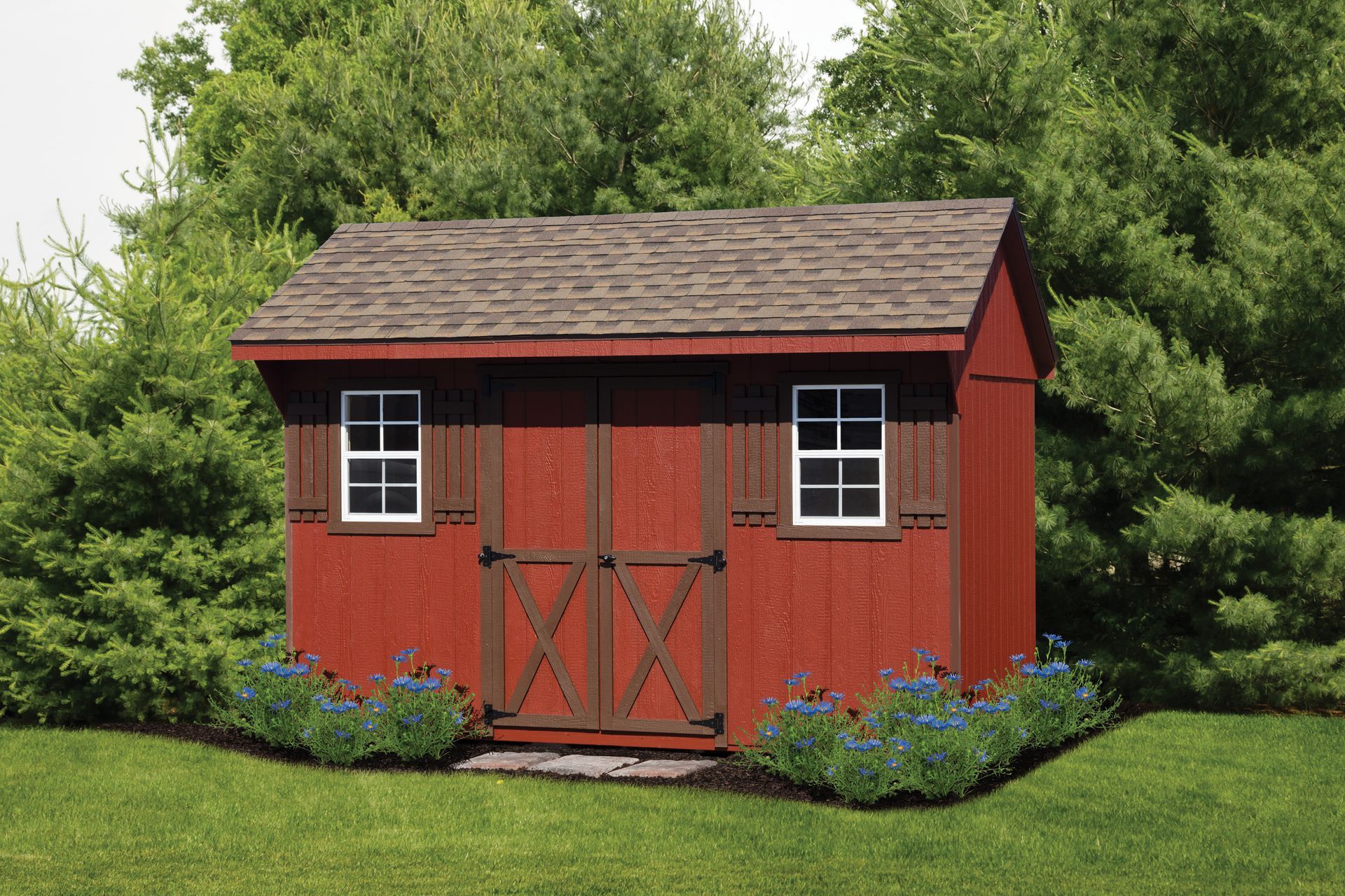 Red garden shed with white-trimmed windows and doors, surrounded by grass, flowers, and trees.