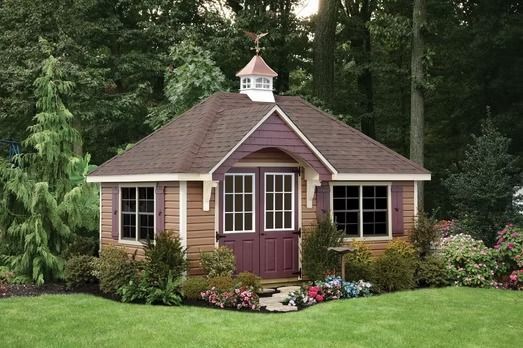 Small tan garden shed with brown roof and flower beds in a lush green yard