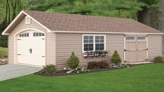 Beige garage with white doors and flower boxes, set beside a grassy lawn and trees.