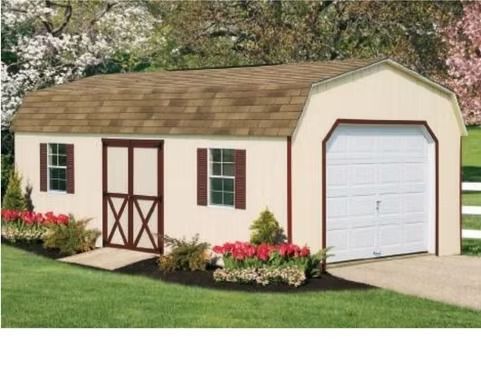 Small beige garden shed with brown trim, white garage door, and flower beds in a grassy yard.