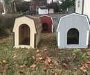 Three small wooden pet shelters in a yard, painted tan, red, and light blue, with fallen leaves around them