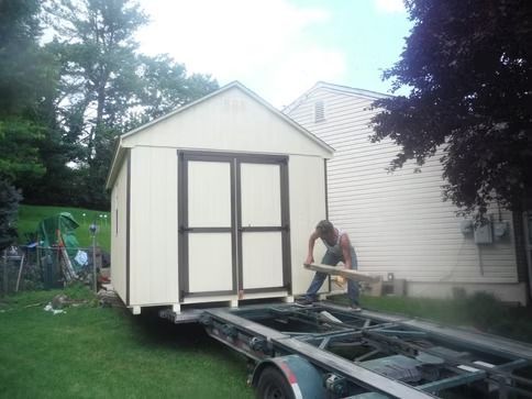 Person working on moving a small white shed onto a trailer in a yard