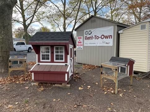 Two small red-and-white shed structures beside a Rent-To-Own sign in a wooded lot