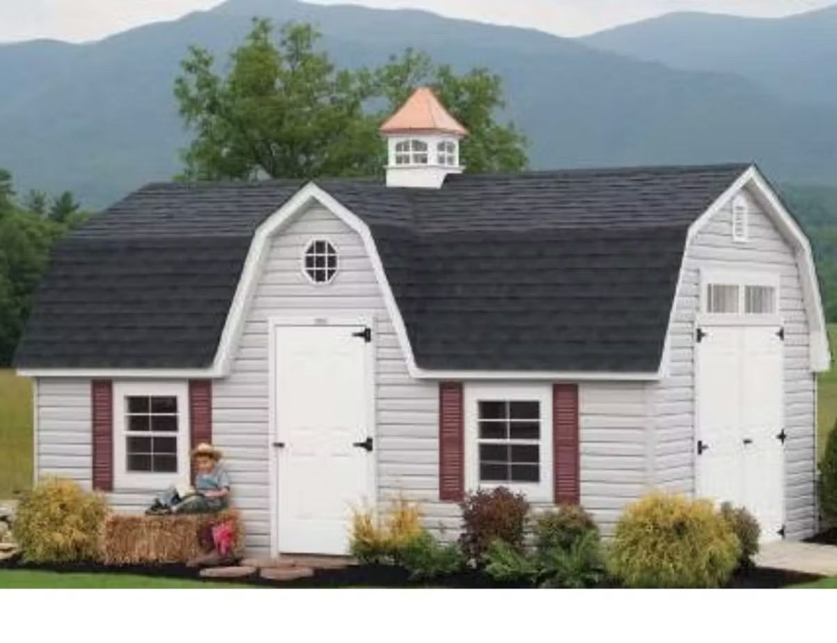Two white garden sheds with black roofs and red shutters in a landscaped yard