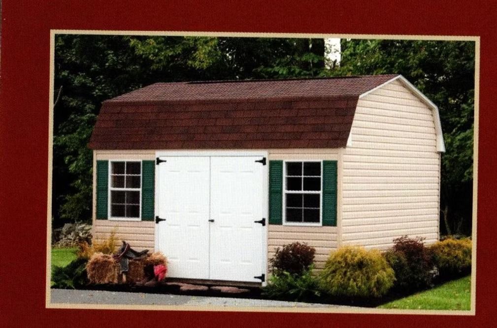 Small white garden shed with brown roof, white double doors, and green-trimmed windows in a landscaped yard