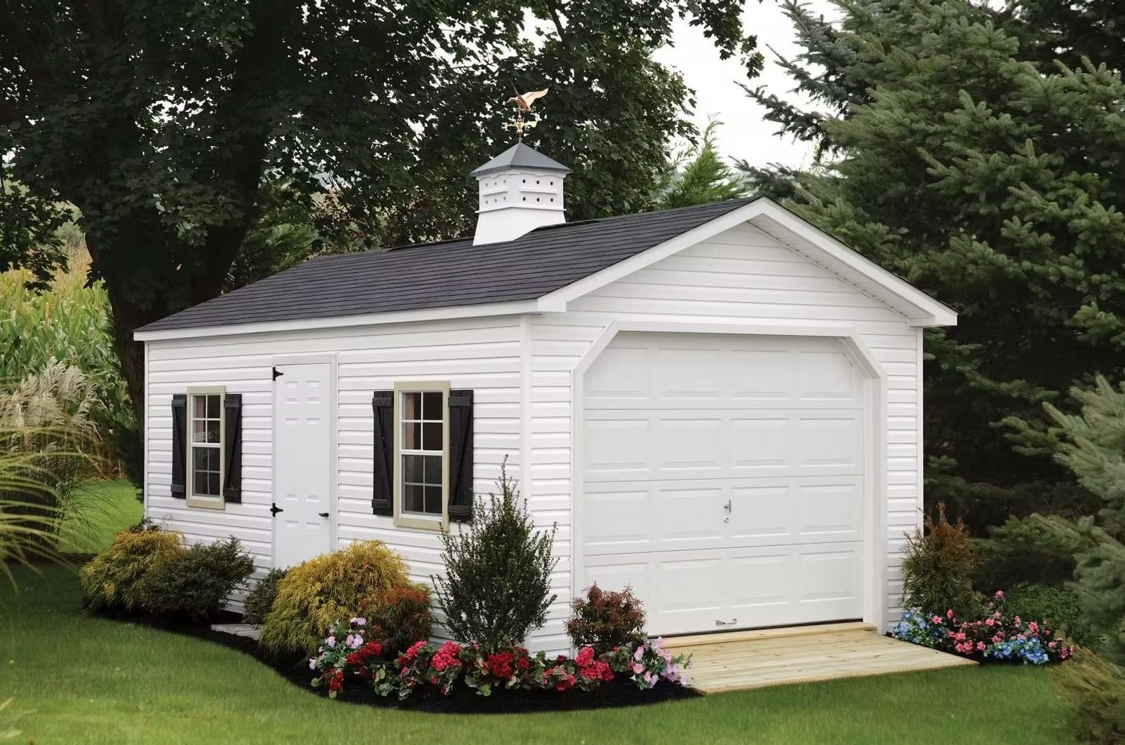 White detached garage with black shutters and flower bed in a green yard.