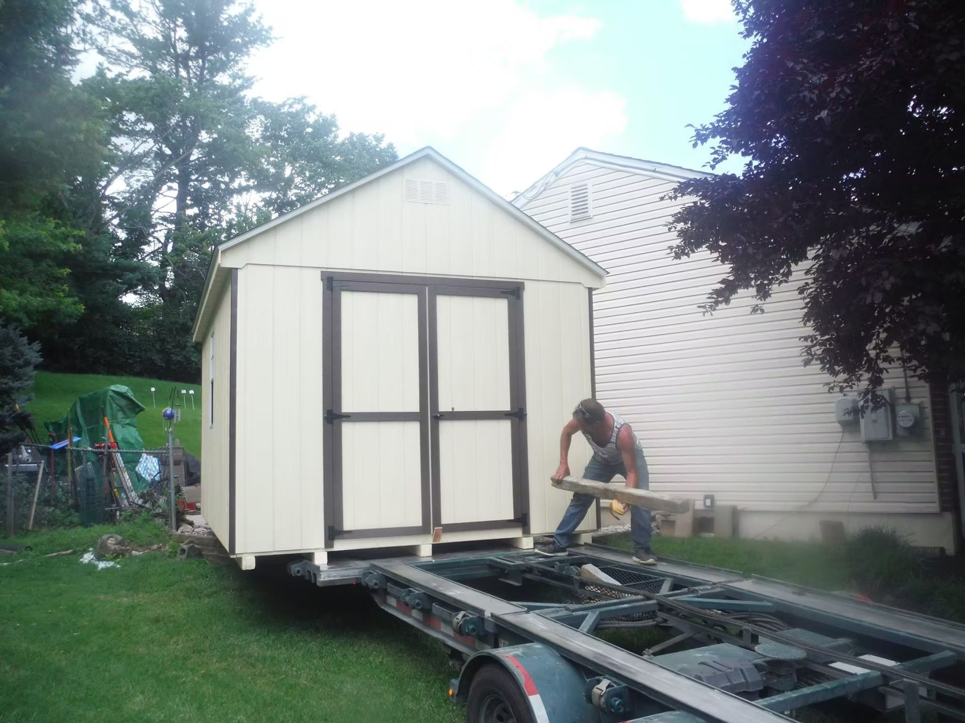 Small white shed being moved on a trailer, with a person working beside it.