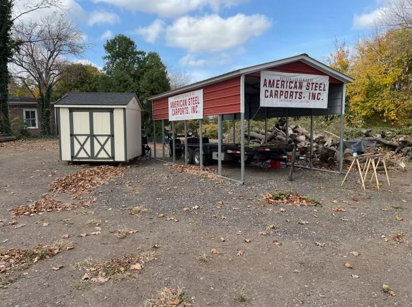 Outdoor farm stand with red canopy, white shed, and pumpkins for sale in a gravel lot in autumn