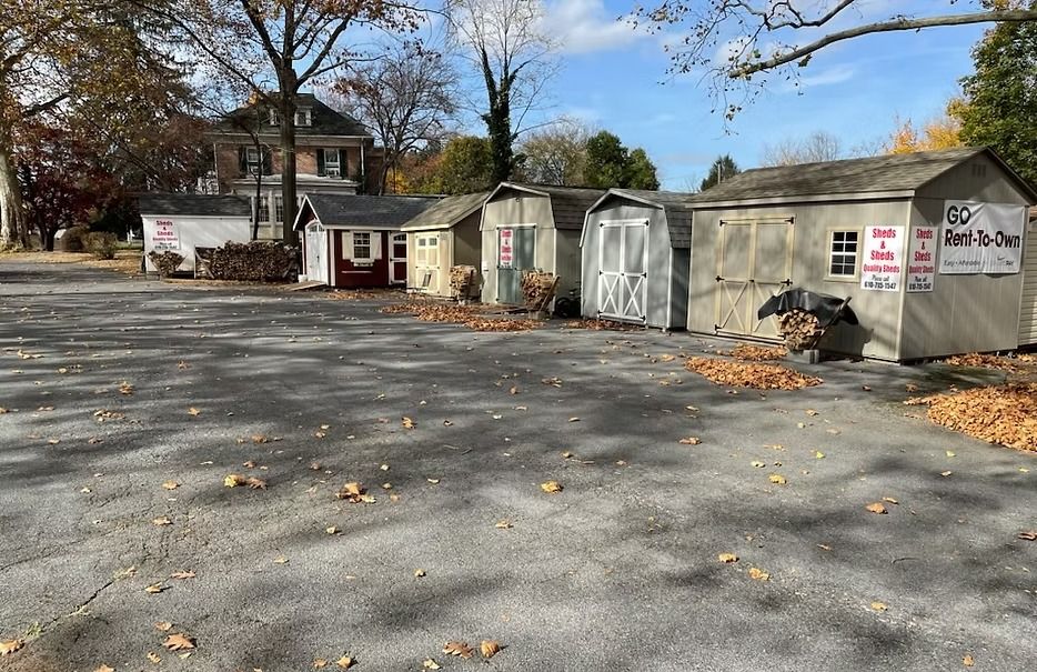 Empty parking lot beside small sheds and buildings under a blue sky with autumn leaves scattered on pavement