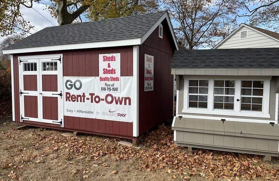Small red rent-to-own shed beside a gray house, with “GO Rent-To-Own” signage.