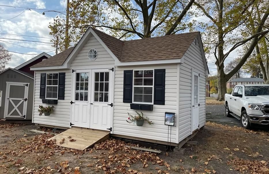 Small white cottage with double doors, black shutters, and a car parked beside it.