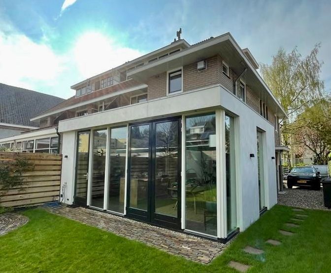 Een groot huis met veel ramen en een auto ervoor geparkeerd.