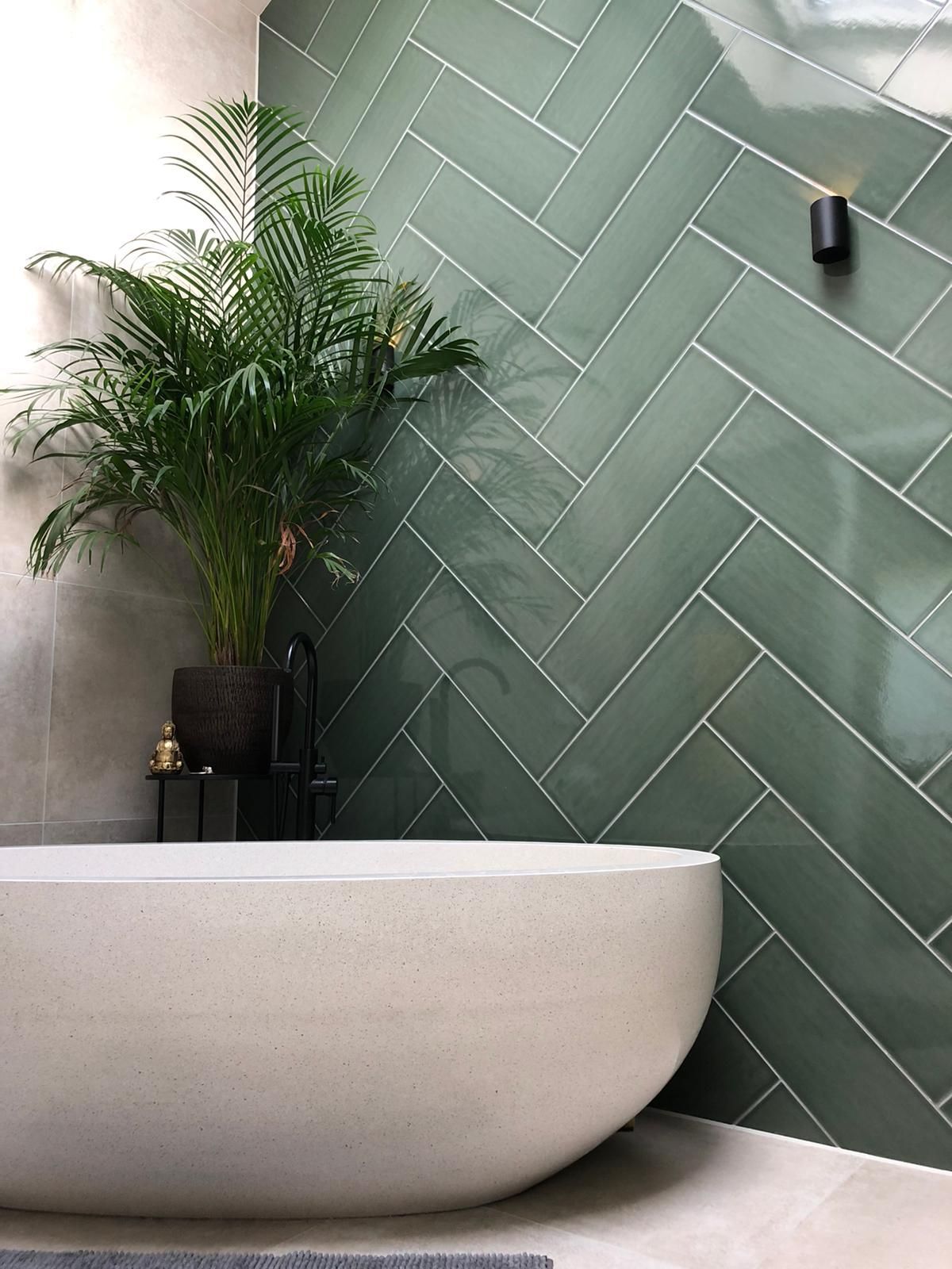 Een badkuip in een badkamer met groene tegels en een plant.
