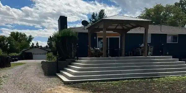 House with large front porch, wide steps, and gravel driveway under a partly cloudy sky