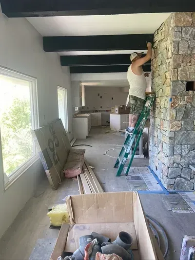 Worker on a ladder installing a stone fireplace in a bright room under renovation