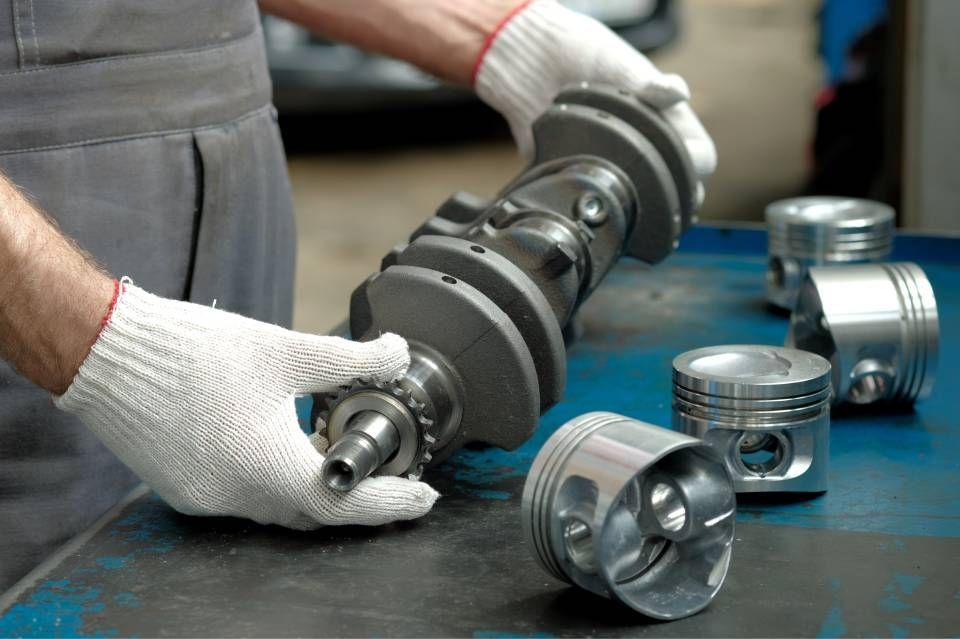 Gloved hands handling a metal crankshaft with pistons on a workshop table