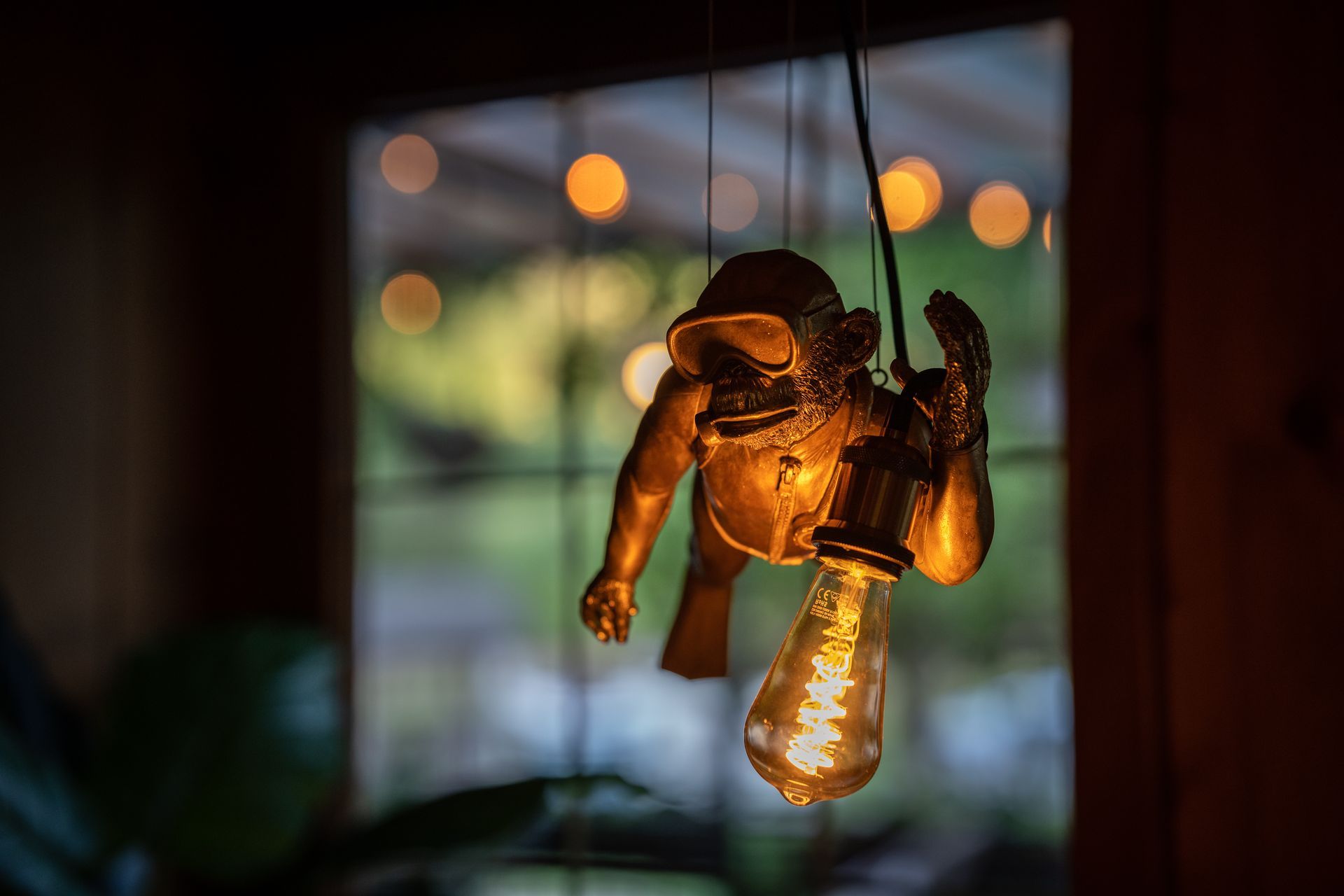 A statue of an astronaut is hanging from the ceiling next to a light bulb.
