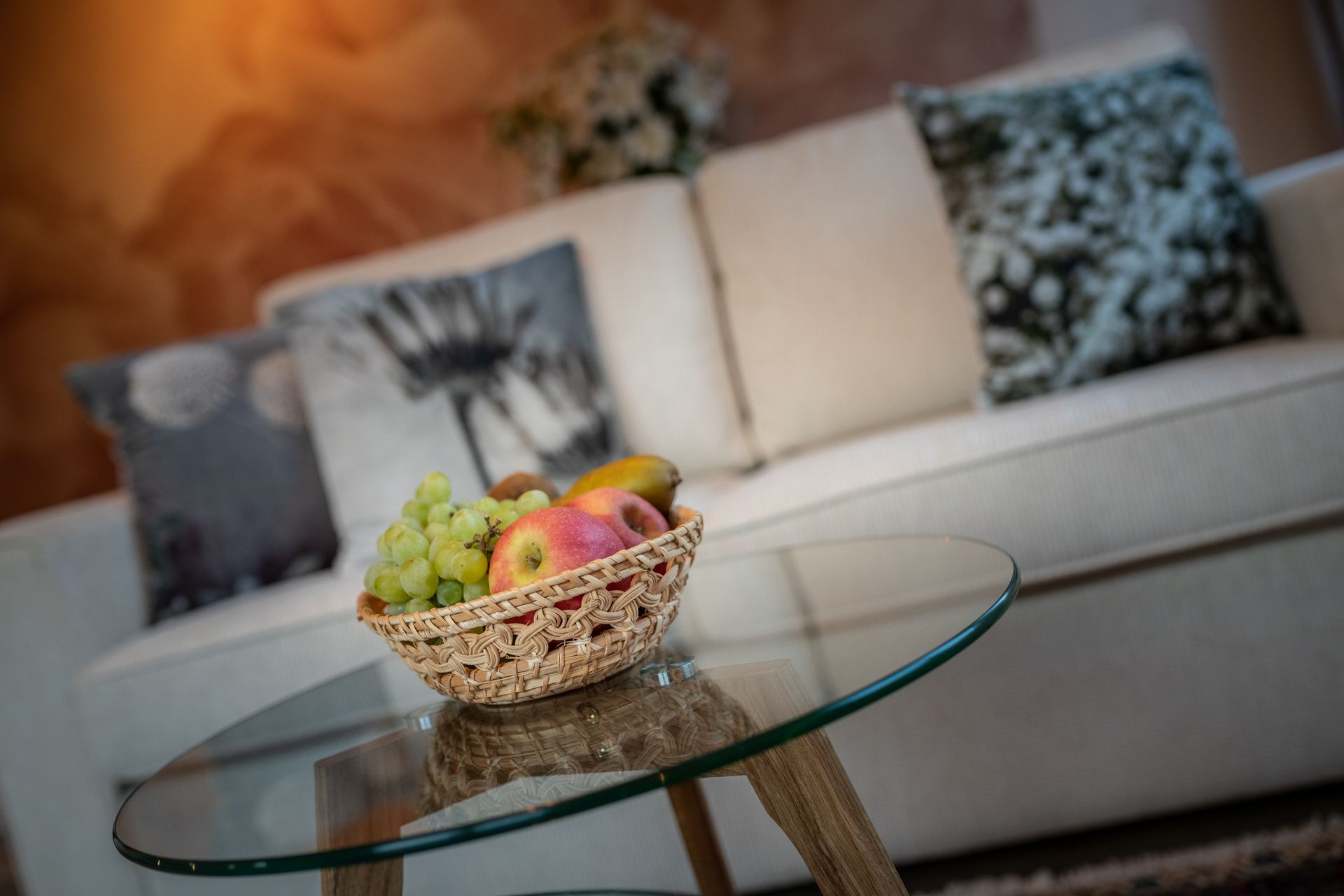 A bowl of fruit is sitting on a glass table in front of a couch.