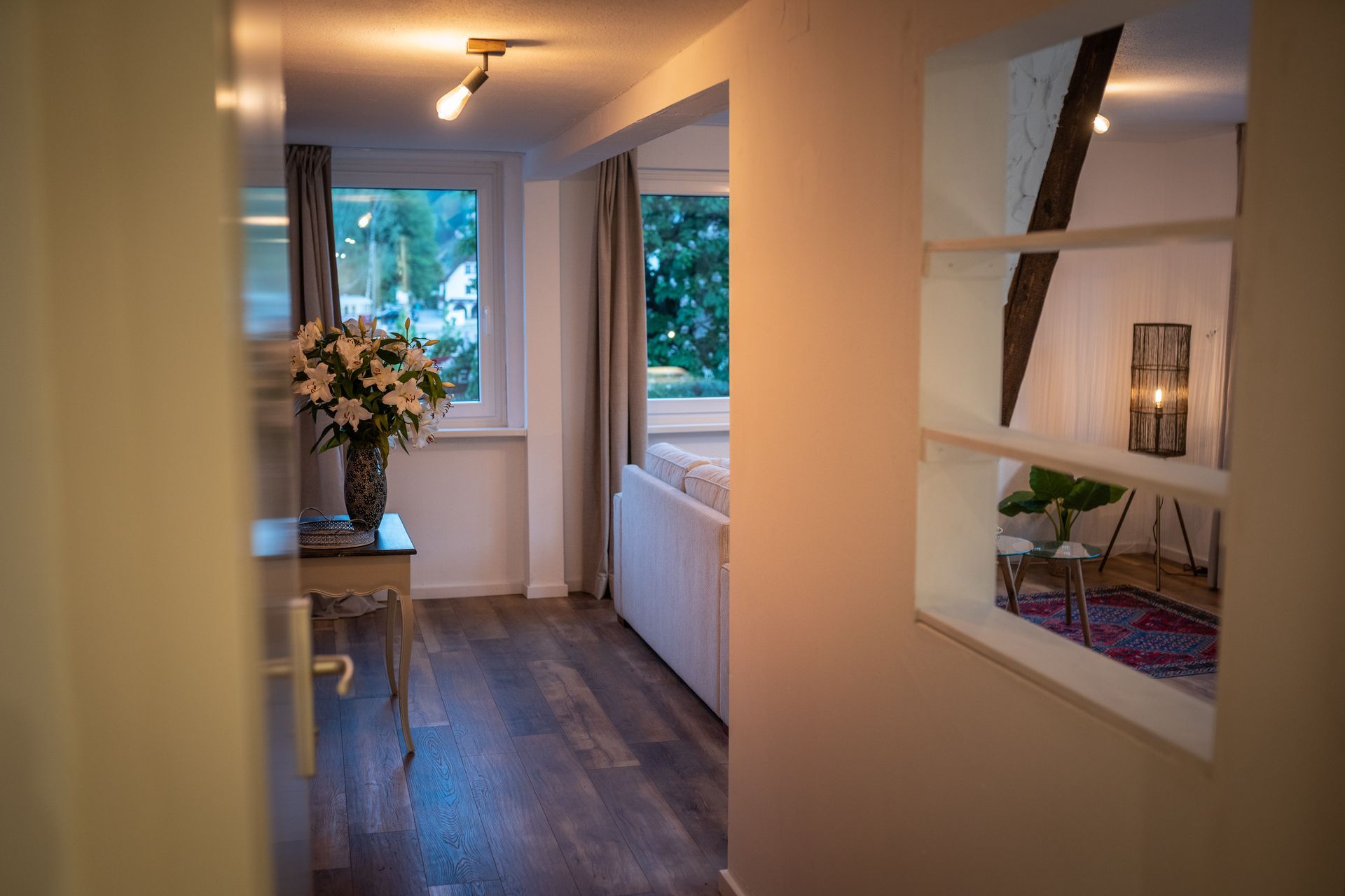 A hallway leading to a living room with a vase of flowers on a table.