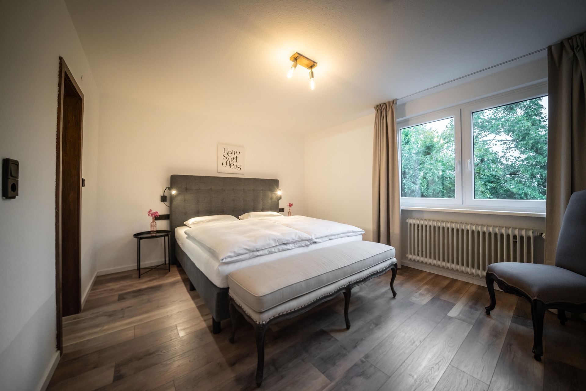 A bedroom with a bed , chair , bench and window.