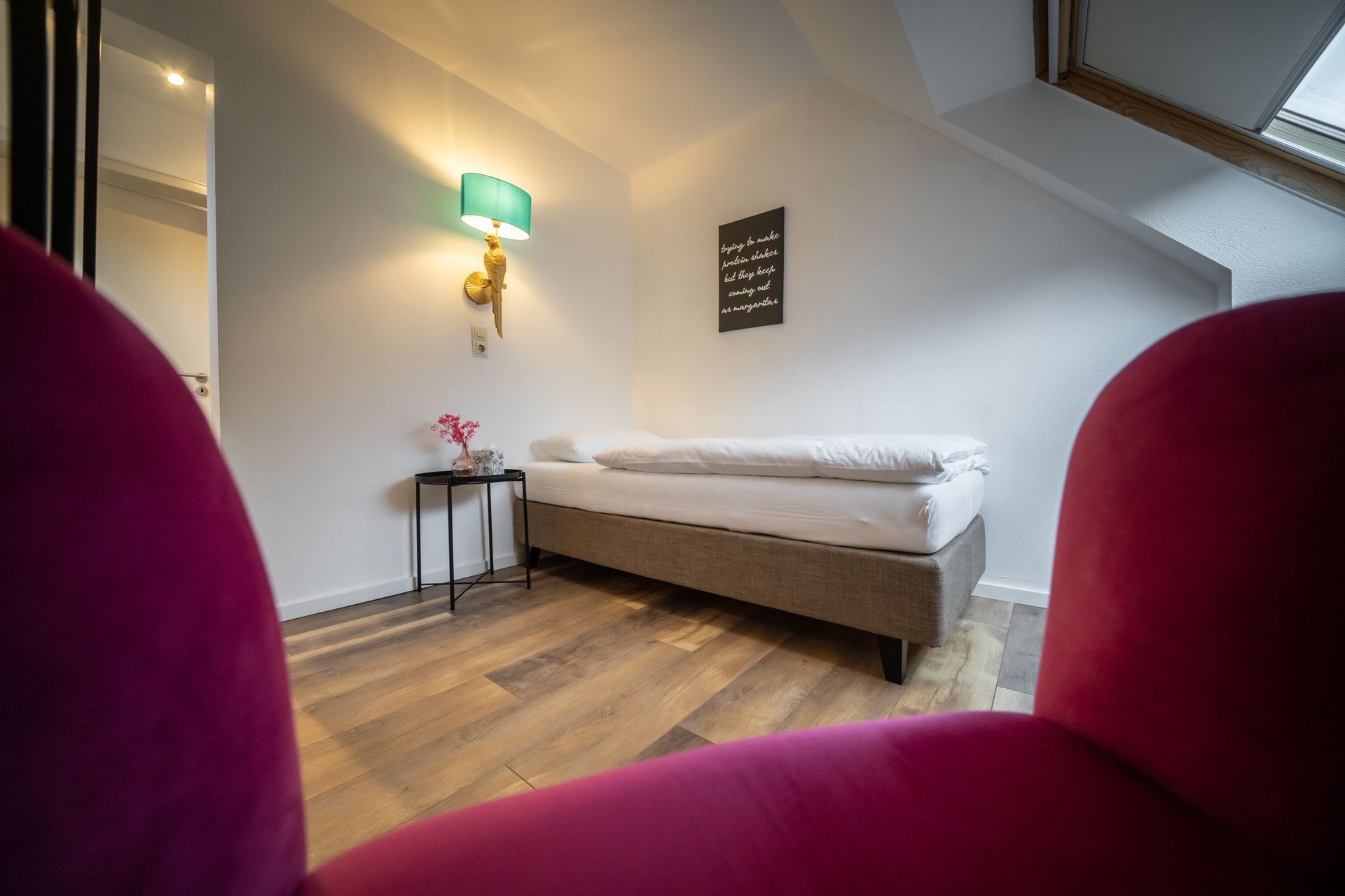 A bedroom with a single bed and a pink chair.