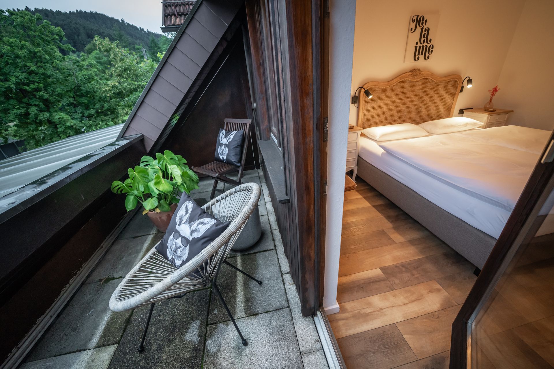 A balcony with a chair and a plant next to a bedroom with a bed.