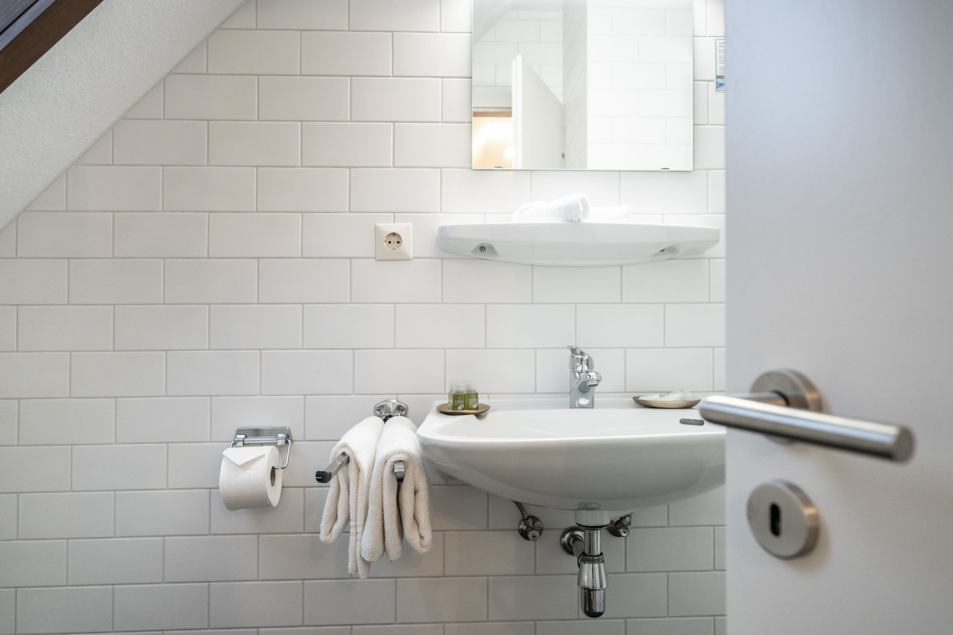 A bathroom with a sink , mirror , toilet paper and towels.