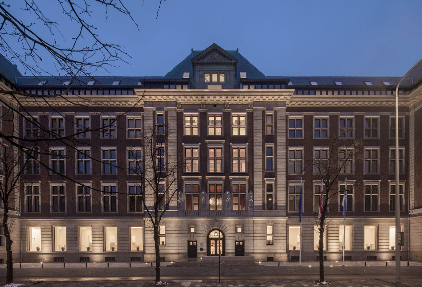 De buitenkant van een bakstenen gebouw, verlicht bij schemering, met meerdere ramen en een gedetailleerde gevel.