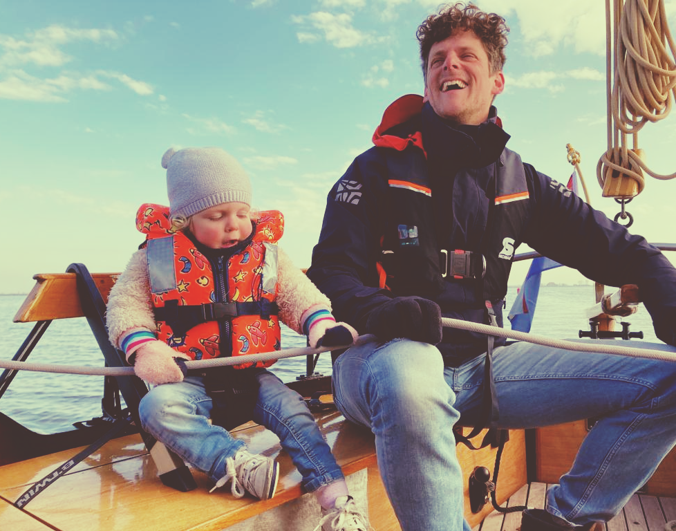 Een man en een kind zeilen, beiden met reddingsvesten aan, en genieten van de vrijheid op het water.