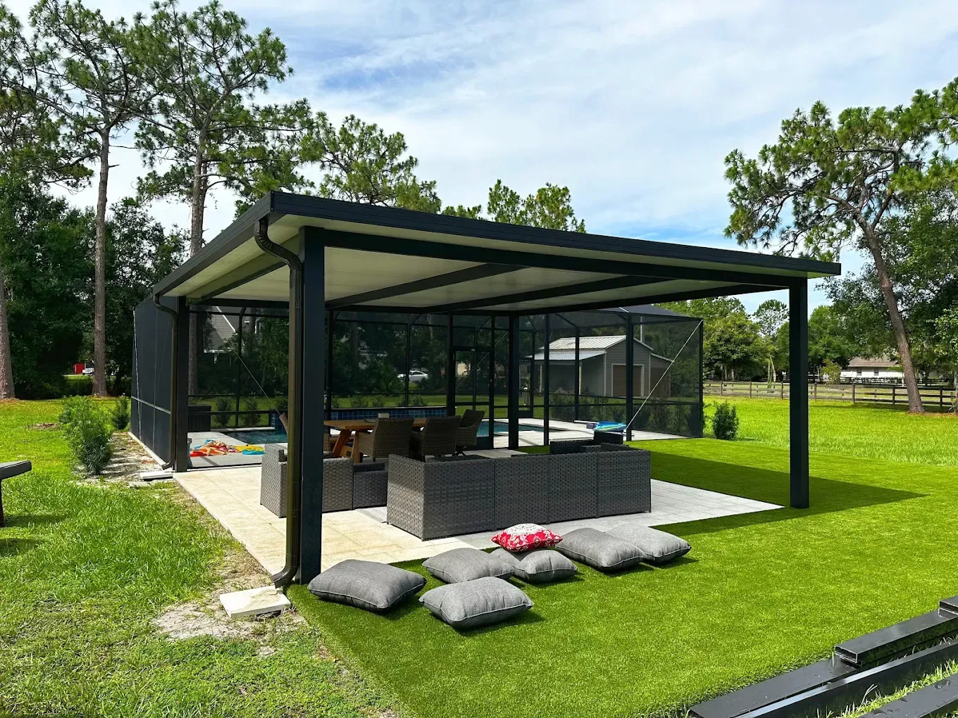 Outdoor living space with a black-framed covered patio, seating, pool screen, and green lawn.