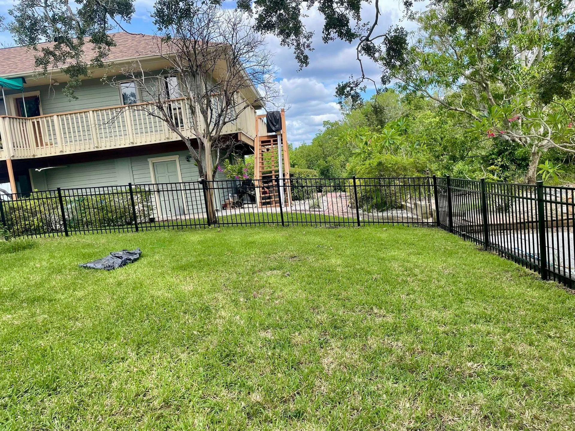 Green grassy backyard with black fence bordering waterway and two-story house with deck.