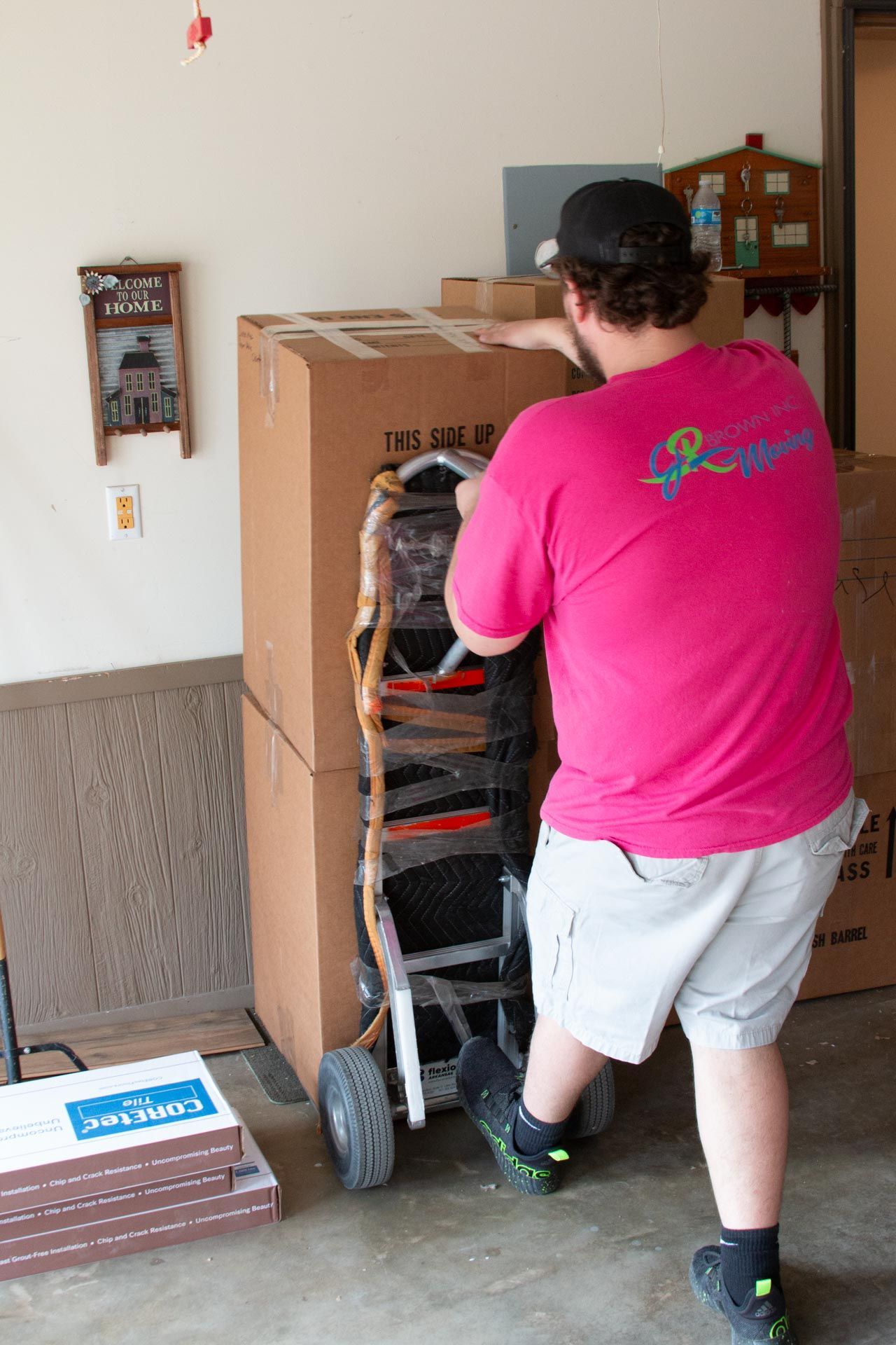 A man in a pink shirt is pushing a cardboard box on a dolly.