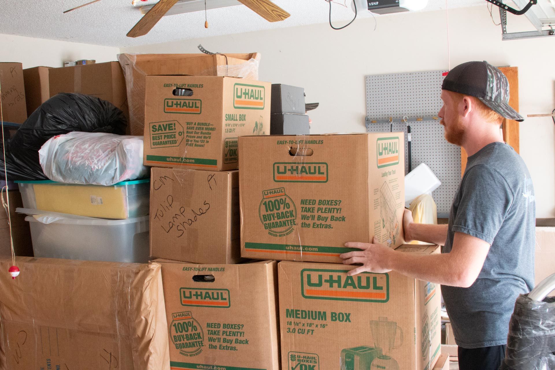 A man is holding a u-haul box in a garage.