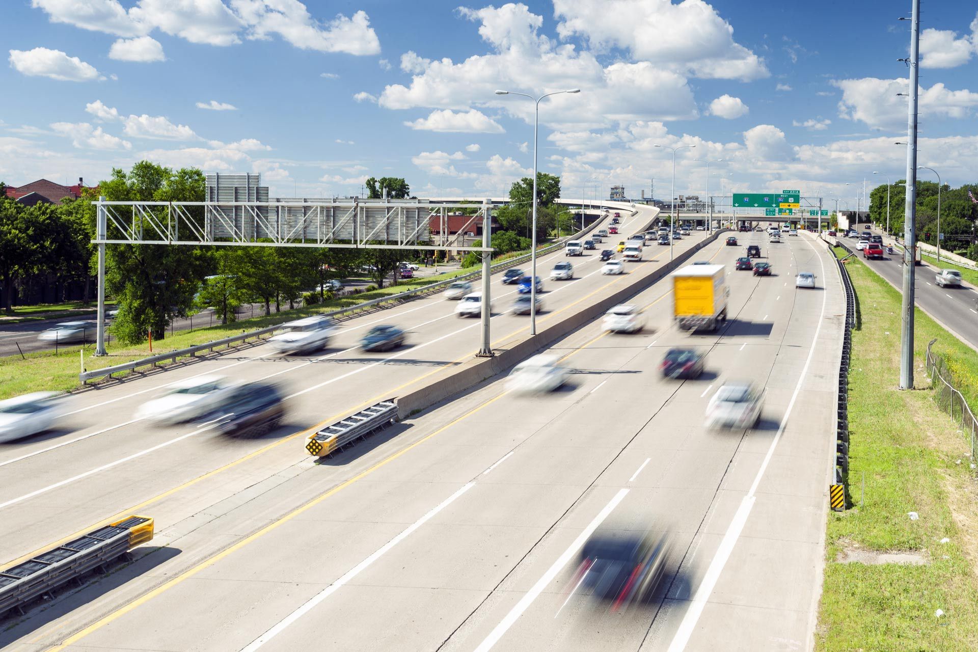 Busy multi-lane highway with moving cars and trucks under a blue sky with clouds