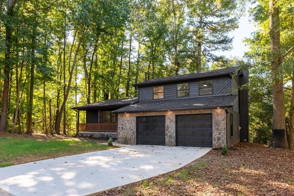 Modern stone house with three-car garage in a wooded driveway setting