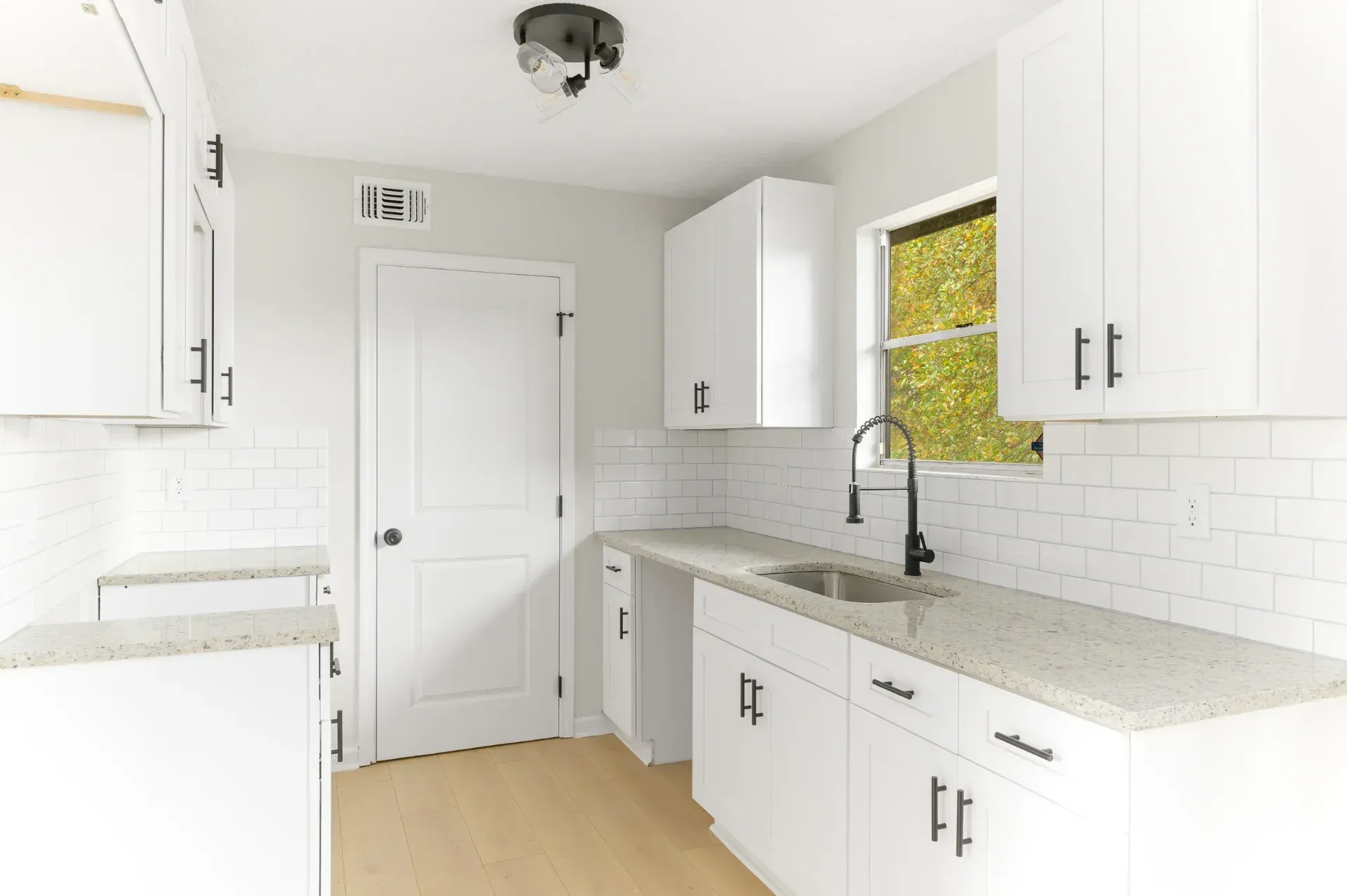 Bright white kitchen with white cabinets, subway tile backsplash, and a window over the sink