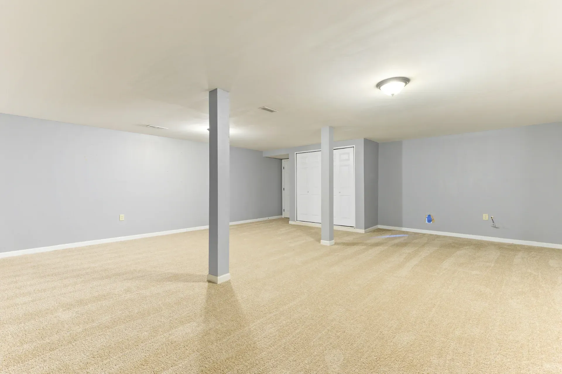 Empty finished basement room with beige carpet, gray walls, and white support columns